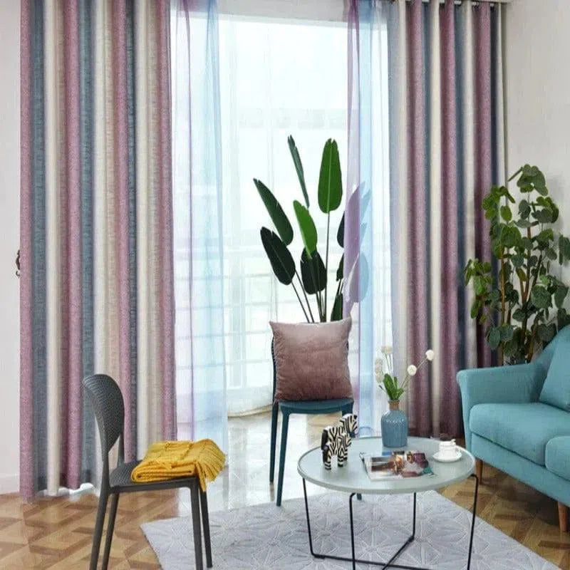 Rideaux multicolores élégants ornant un salon moderne, avec une décoration intérieure harmonieuse comprenant un canapé bleu, un fauteuil assorti, et une table basse contemporaine agrémentée d'objets décoratifs. La pièce est illuminée par une lumière naturelle venant de grandes fenêtres avec des rideaux semi-transparents, créant une ambiance chaleureuse et accueillante.