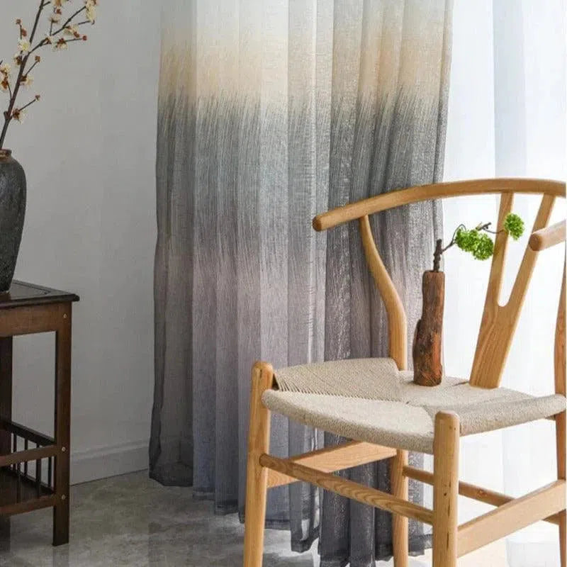 Photographie d’un intérieur minimaliste avec une chaise en bois au design épuré, posée devant un rideau dégradé gris et blanc. Ambiance zen et déco élégante pour un salon moderne et raffiné.