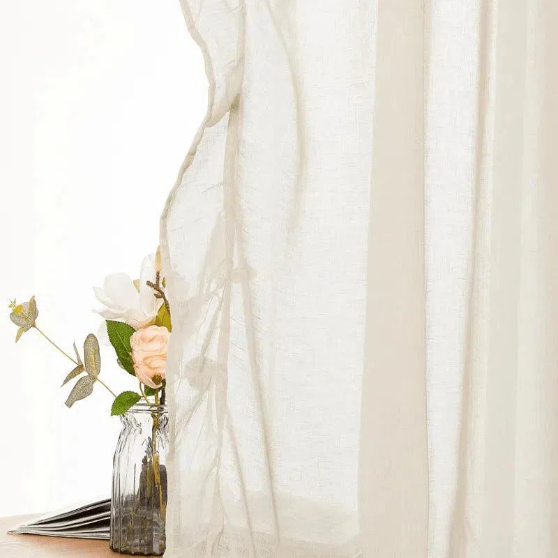 Voilage élégant beige pour salon moderne, laissant filtrer une douce lumière naturelle, avec vase décoratif et fleurs délicates en arrière-plan. Optimisé pour un intérieur chaleureux et accueillant.