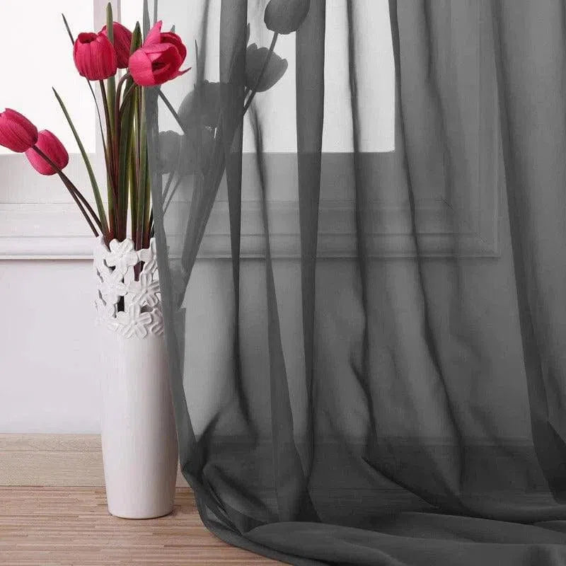 Rideau translucide élégant de couleur noire, parfait pour ajouter une touche de sophistication à votre intérieur. Accompagné d’un vase décoratif blanc avec des fleurs rouges, il crée un contraste visuel saisissant. Idéal pour le salon ou la chambre, ce rideau permet à la lumière de filtrer doucement tout en préservant l'intimité. Accessoire décoratif essentiel pour une maison moderne et stylée.
