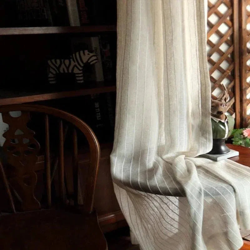 Rideau finement rayé, idéal pour décorer un intérieur avec élégance et douceur. Parfait pour créer une ambiance chaleureuse et accueillante dans votre salon ou chambre. Agencement harmonieux avec une chaise en bois et une étagère, mettant en valeur un style classique et raffiné. Accessoire de décoration incontournable pour filtrer la lumière tout en préservant l'intimité.