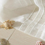 Drap blanc léger disposé sur un sol en bois clair, décoré avec des coquillages marins. Ambiance estivale et bord de mer, parfait pour une décoration intérieure fraîche et naturelle. Accessoire idéal pour apporter une touche de douceur et d'élégance à votre espace.